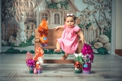 Charmant bébé en robe rose entouré de décors de Pâques, assis sur un banc en bois